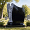 Black granite angel headstone with leaning carved angel viewed in a cemetery