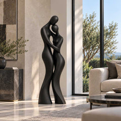 Matte black abstract bronze couple sculpture displayed beside a sofa in a modern living room