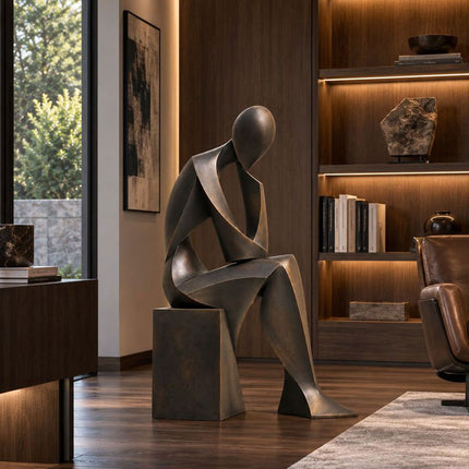 Abstract seated figure sculpture with a dark bronze finish displayed in a modern home study.