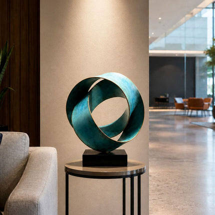 Blue-green bronze abstract sculpture displayed on a round side table beside a sofa in a modern interior