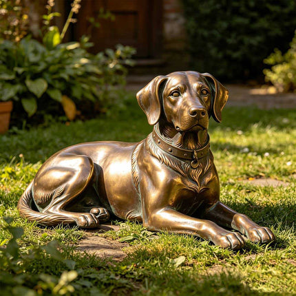 Bronze dog statue resting on the grass in a landscaped private garden.