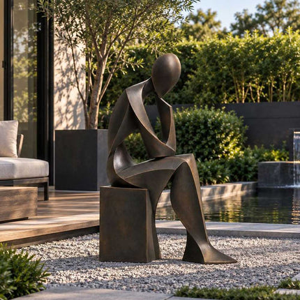 Dark bronze seated figure sculpture displayed in a private garden beside a modern swimming pool.