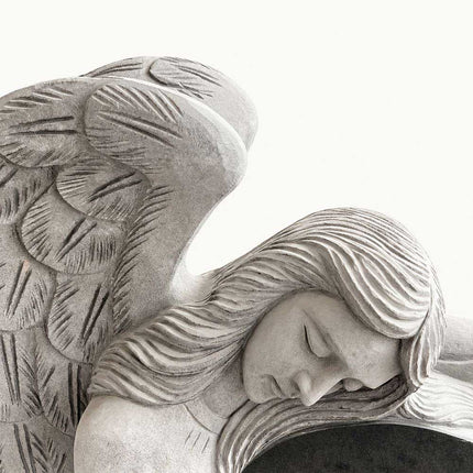 Close view of the carved angel resting against the heart-shaped granite headstone