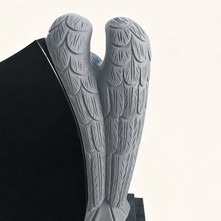 Carved feathered angel wings on the side of a black granite headstone