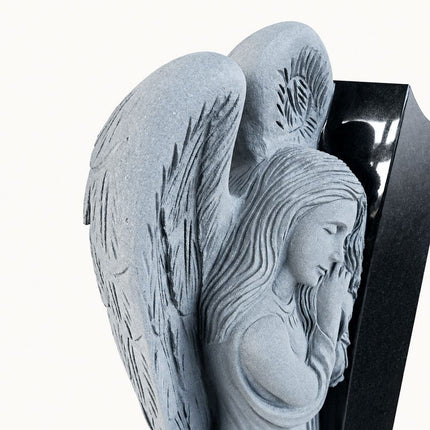 Carved leaning angel with lowered head and folded hands on a black granite headstone