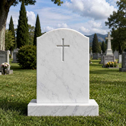 Curved-top white marble Christian headstone with a recessed cross in a landscaped cemetery