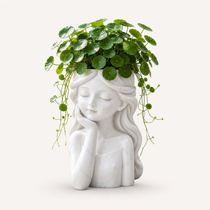 White stone girl head planter with closed eyes, flowing hair, and green plants growing from the open top