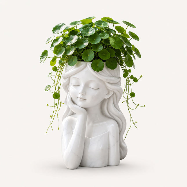 White stone girl head planter with closed eyes, flowing hair, and green plants growing from the open top