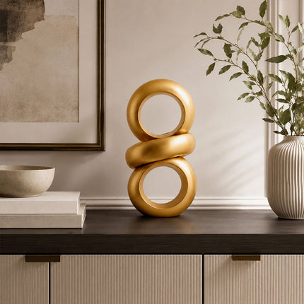 Gold abstract ring sculpture displayed on a dark wood console in a modern interior
