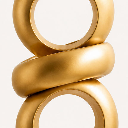 Front detail of a gold abstract sculpture showing two circular openings and a diagonal connecting band