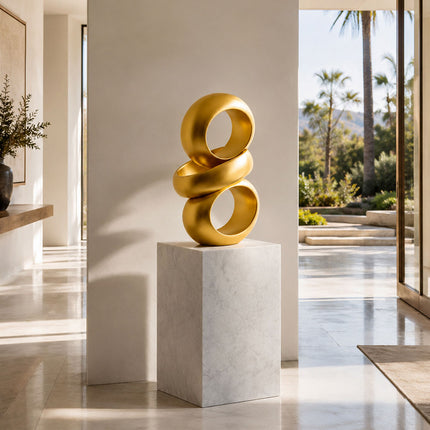 Gold abstract ring sculpture displayed on a white stone pedestal in a contemporary home