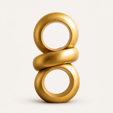 Gold abstract ring sculpture with two vertical circular loops and a diagonal central band on a white background