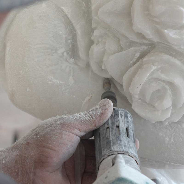 Hand carving intricate floral details on a white marble sculpture using traditional sculpting techniques.