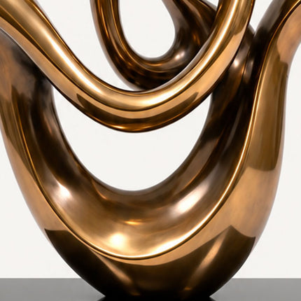 Close-up of the smooth reflective bronze-tone finish and sweeping lower curves of the stainless steel sculpture.