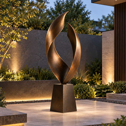 Modern bronze sculpture with flowing open form displayed in a softly lit courtyard