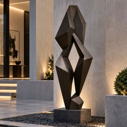 Modern geometric bronze sculpture with faceted surfaces in an outdoor architectural setting
