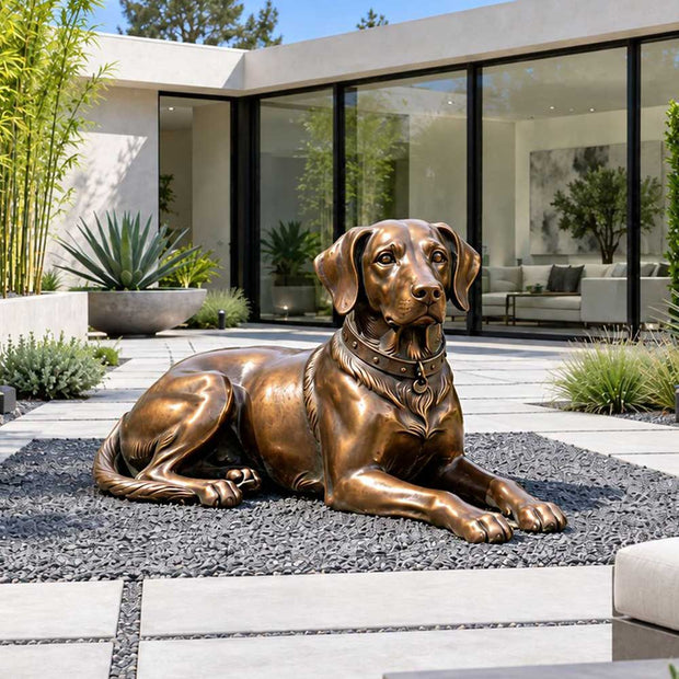Reclining bronze dog sculpture displayed in a gravel garden within a modern residential courtyard.