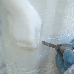 An artisan refining the drapery of a handcrafted white marble sculpture to achieve crisp folds and smooth transitions before polishing.