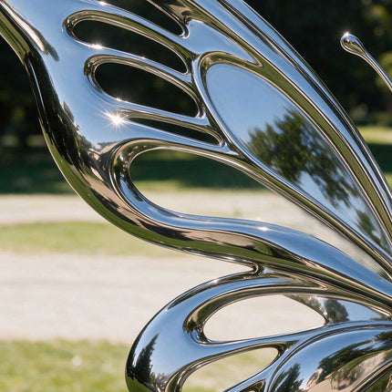 Close-up of the butterfly sculpture's polished stainless steel wing showing elongated openings and reflective curved edges.