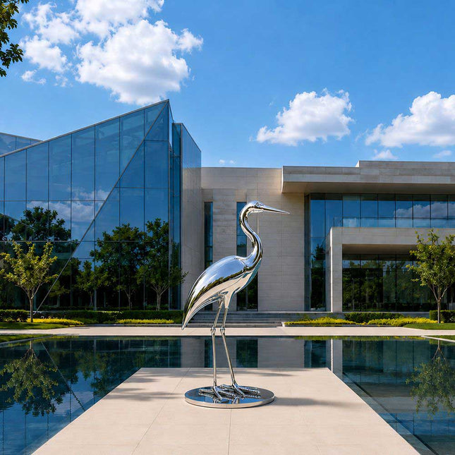 Stainless steel heron sculpture installed in a modern architectural landscape with water feature