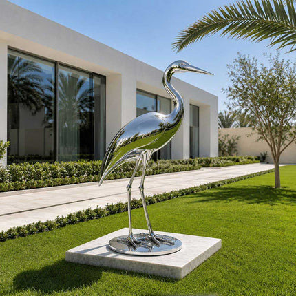Polished stainless steel heron sculpture placed in a contemporary garden landscape