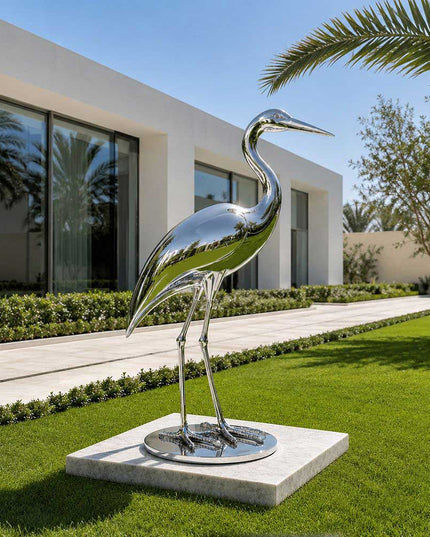 Polished stainless steel heron sculpture placed in a contemporary garden landscape