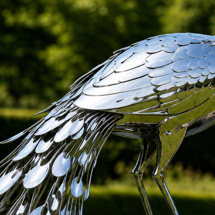 Close-up of layered stainless steel wing feathers and oval tail details on a mirror polished peacock sculpture