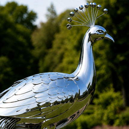 Close-up of a mirror polished stainless steel peacock sculpture showing its curved neck, beak, eyes, and radiating crest