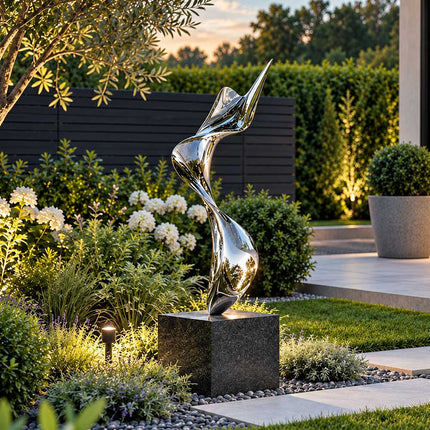 Mirror polished stainless steel ribbon sculpture on a dark stone pedestal in a landscaped private garden