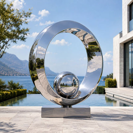 Mirror polished stainless steel ring sculpture beside a luxury waterfront residence and swimming pool.