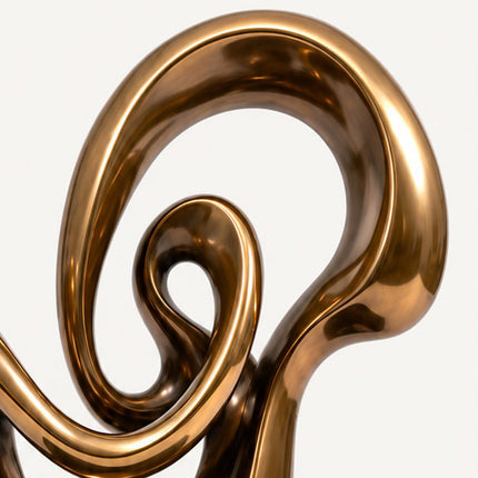Close-up of the open spiral loops and mirror polished bronze-tone surface of an abstract stainless steel sculpture.