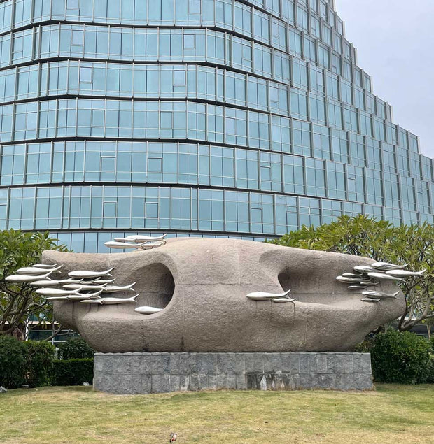 Stone sculpture with stainless steel fish in a landscaped outdoor setting